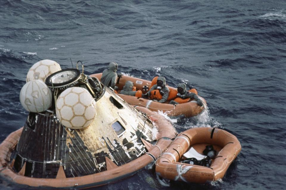 Two small dinghies, one full of crew members, float next to a metal capsule.